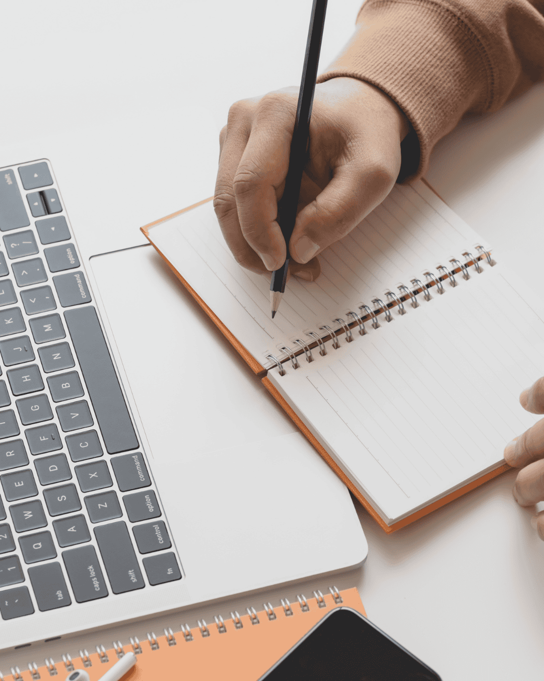 A person writing in a notebook beside a laptop